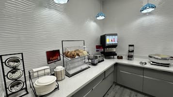 A modern breakfast area with a self-serve station, a display of pastries, and a coffee machine.