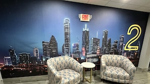 Una habitación con dos sillones estampados, una mesita redonda y un mural con un paisaje urbano que incluye un letrero de salida y el número 2 grande.