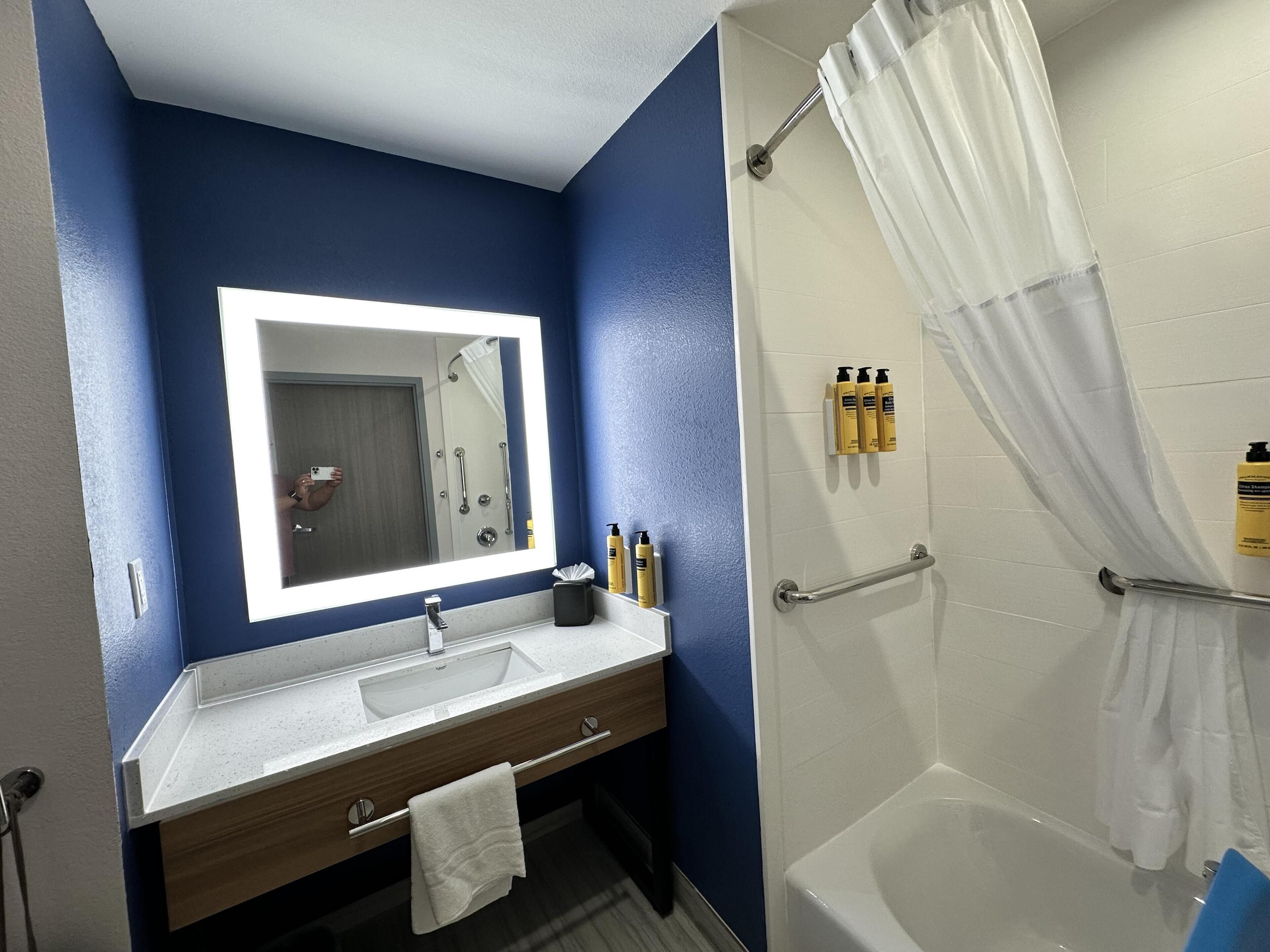 Baño con lavabo, espejo, ducha y artículos de aseo.
