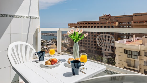 A balcony with a table set for breakfast, a vase with flowers, and a view of buildings and water. - AS EXT Fgrl PYR 1004 (Fuengirola)