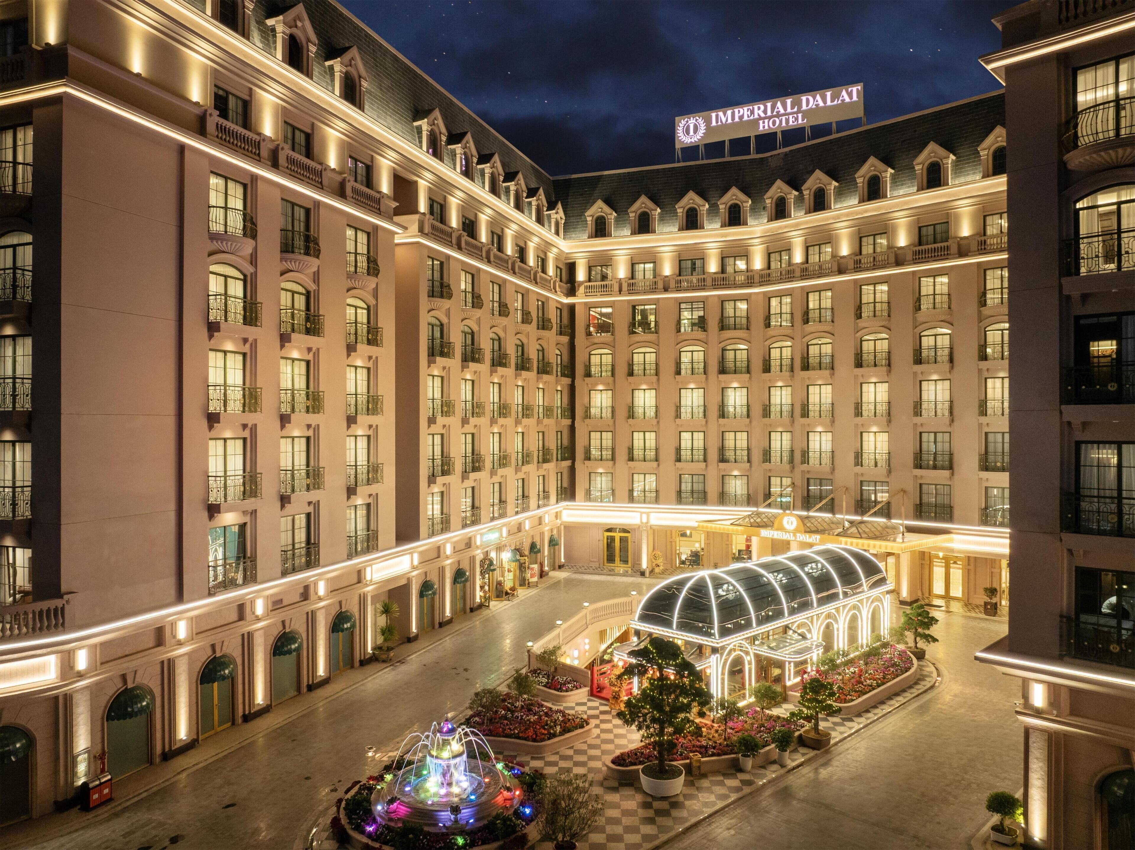 A multi-story hotel with a central courtyard, a fountain, and a glass greenhouse structure.