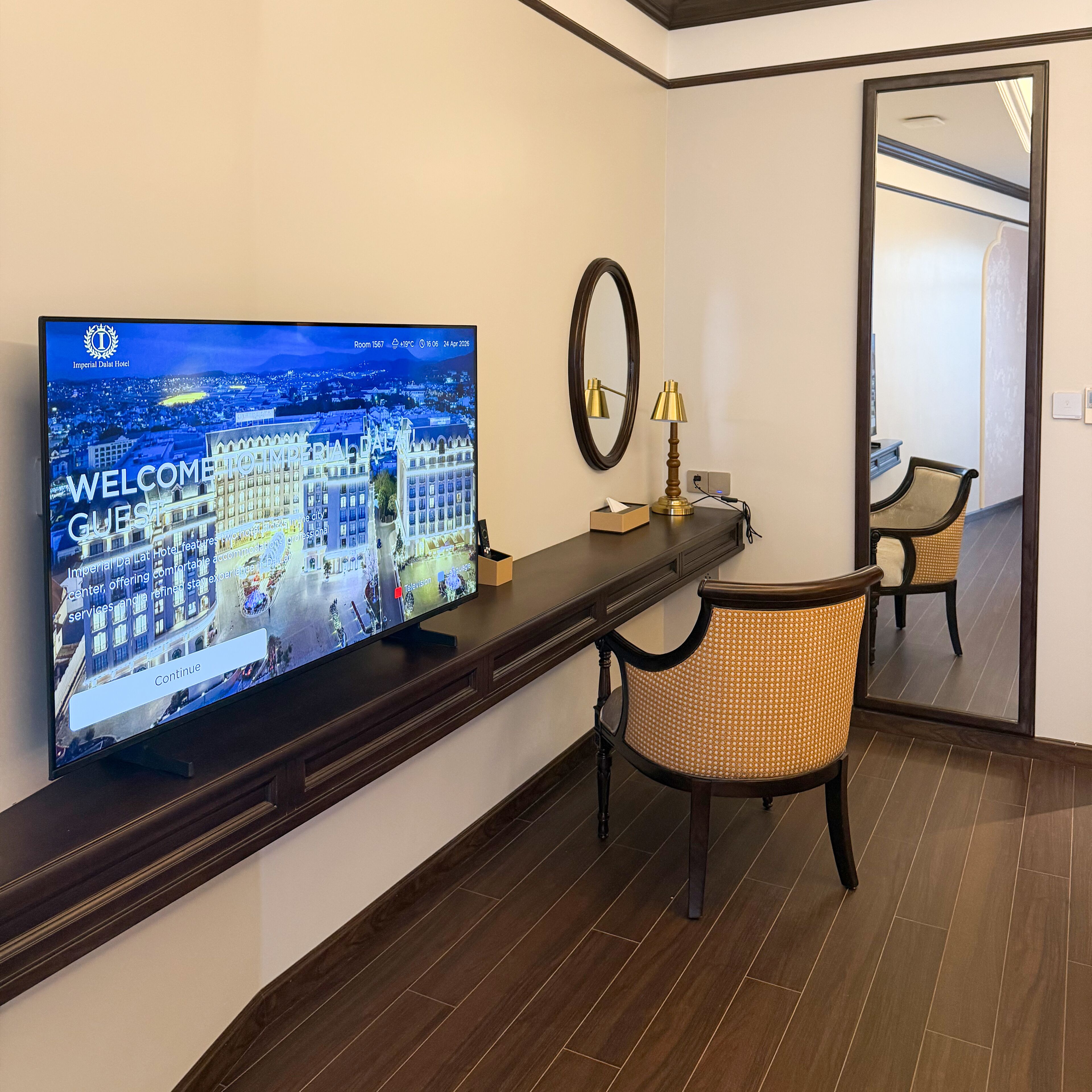 Une chambre d’hôtel équipée d’une télévision affichant un écran d’accueil, d’un miroir, d’une lampe et d’une chaise.