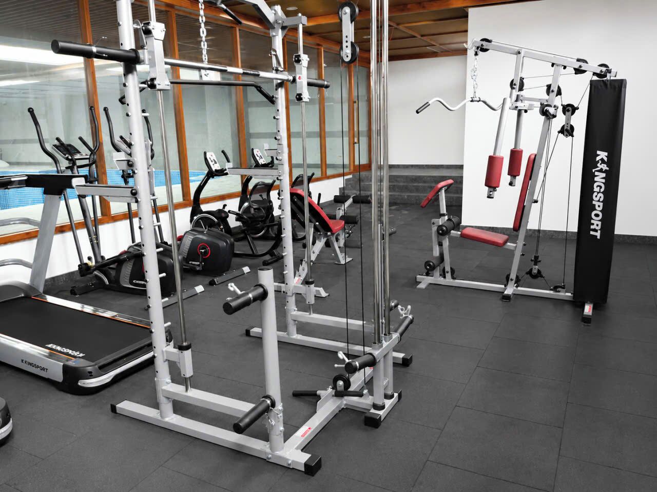 Une salle de sport équipée de divers appareils d’exercice, notamment des tapis de course, des appareils de musculation et un banc.