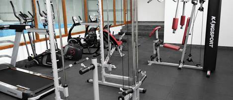 Un gimnasio con diferentes equipos de ejercicio, incluyendo cintas de correr, máquinas de pesas y una banca.