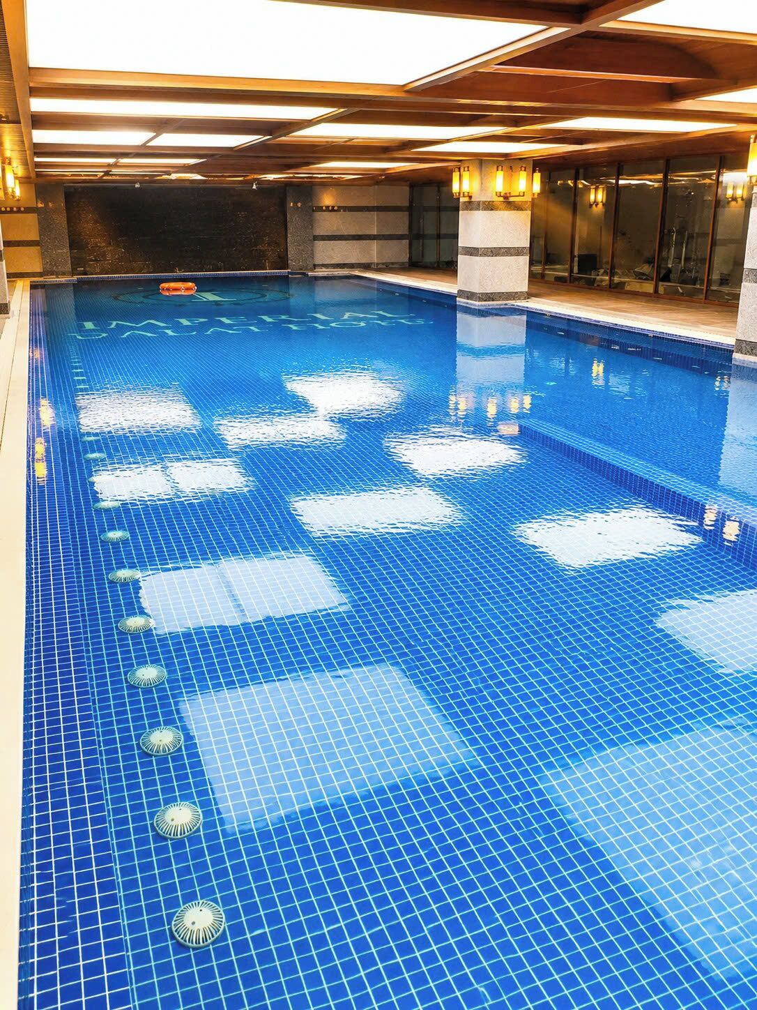 A large indoor swimming pool with clear blue water, tiled floor, and overhead lighting.