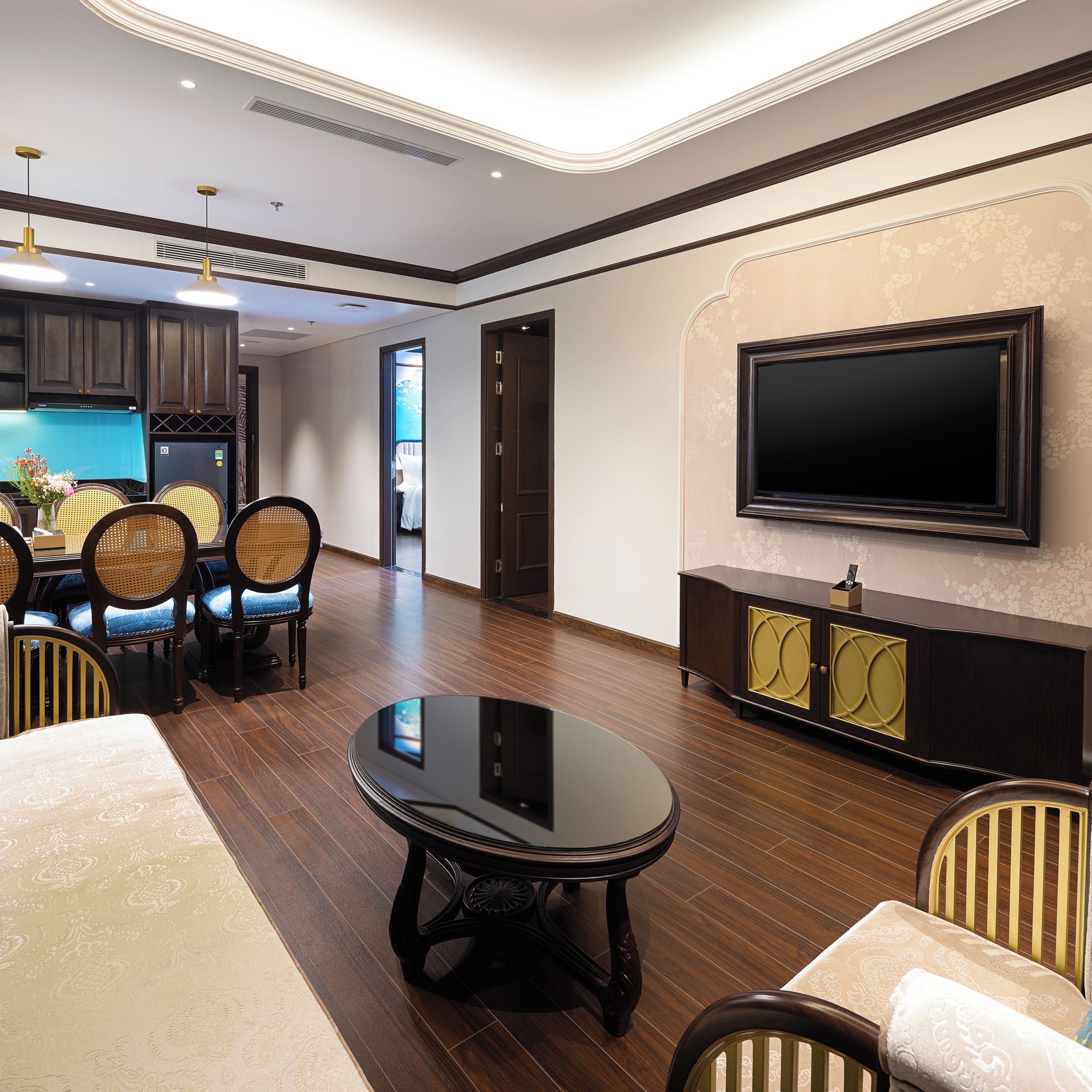 A modern living room with a dining area, wooden flooring, and a large flat-screen TV mounted on the wall.