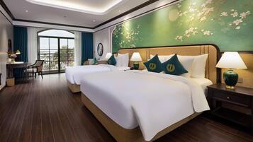 Ein Hotelzimmer mit zwei Betten, einem Schreibtisch, einem Sessel und Balkonblick.