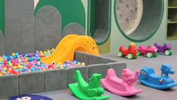 Un espace de jeux pour enfants avec une piscine à balles, un toboggan et des véhicules jouets.
