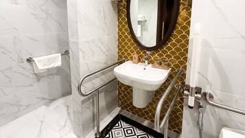 Un baño con piso de mármol, lavamanos con resalte dorado, espejo y zona de ducha.