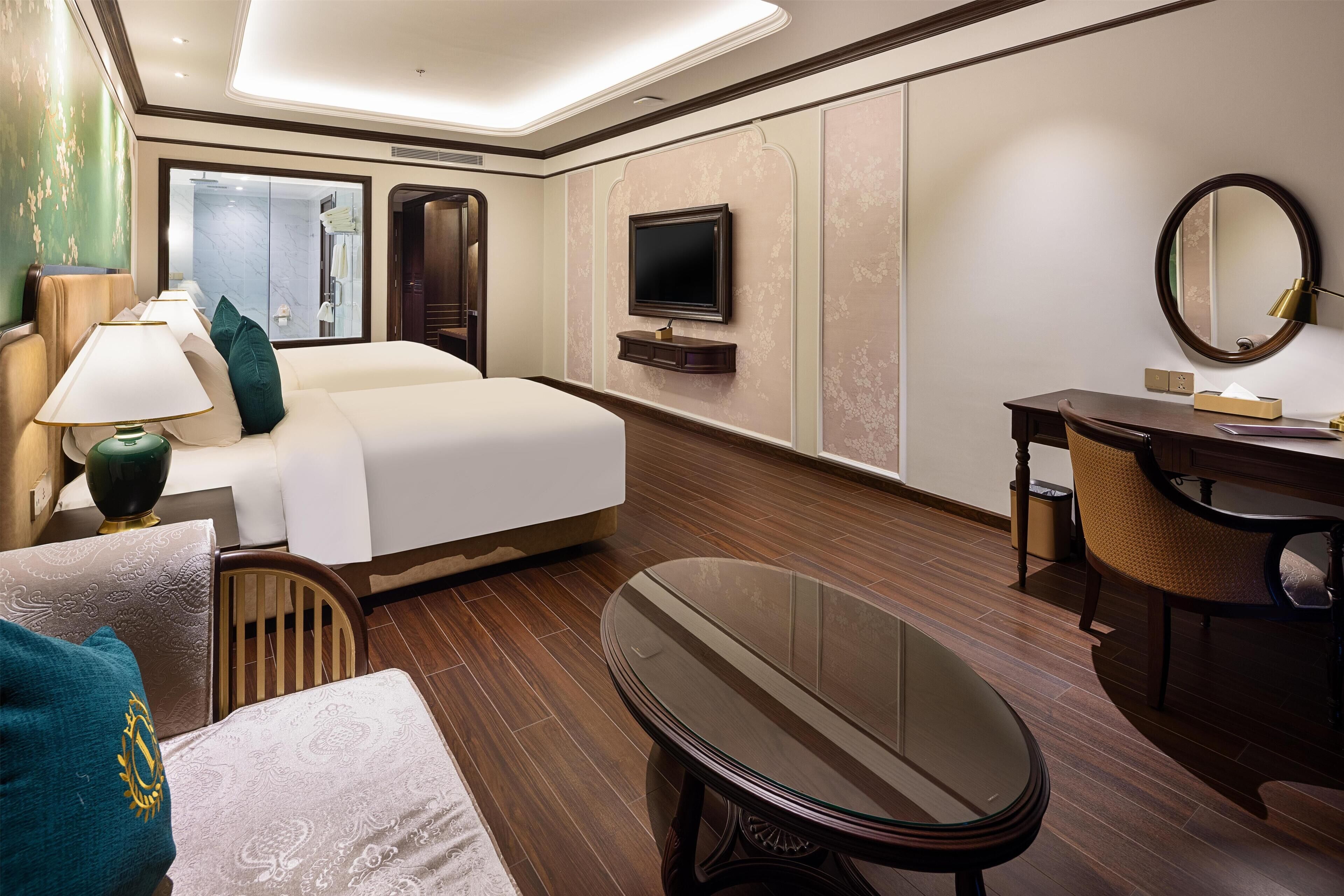 A hotel room with a bed, a desk, a chair, a TV, and a mirror.