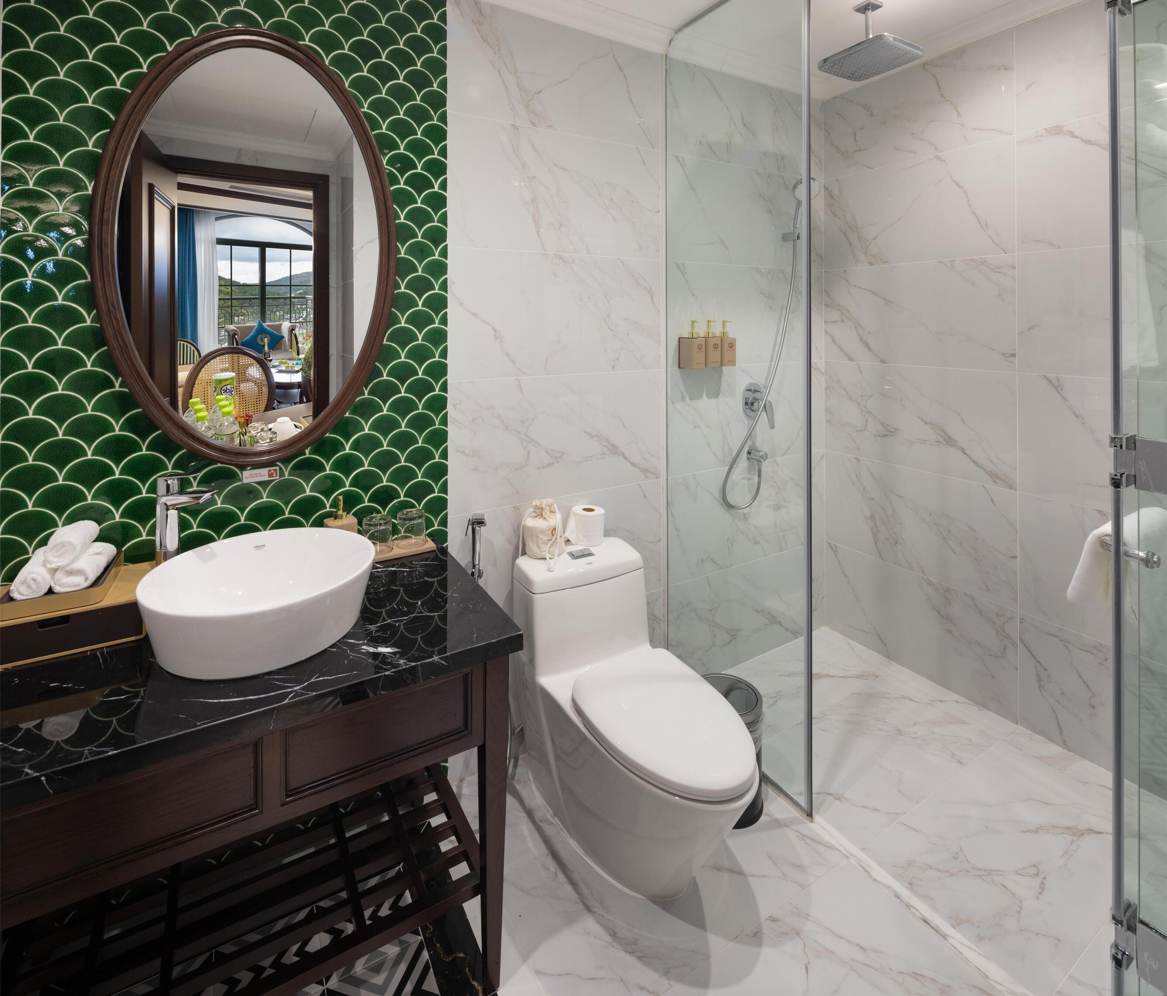 Un baño con un lavamanos blanco, un inodoro, una ducha con puerta de cristal y una pared de azulejos verdes.