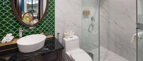 Un baño con un lavamanos blanco, un inodoro, una ducha con puerta de cristal y una pared de azulejos verdes.