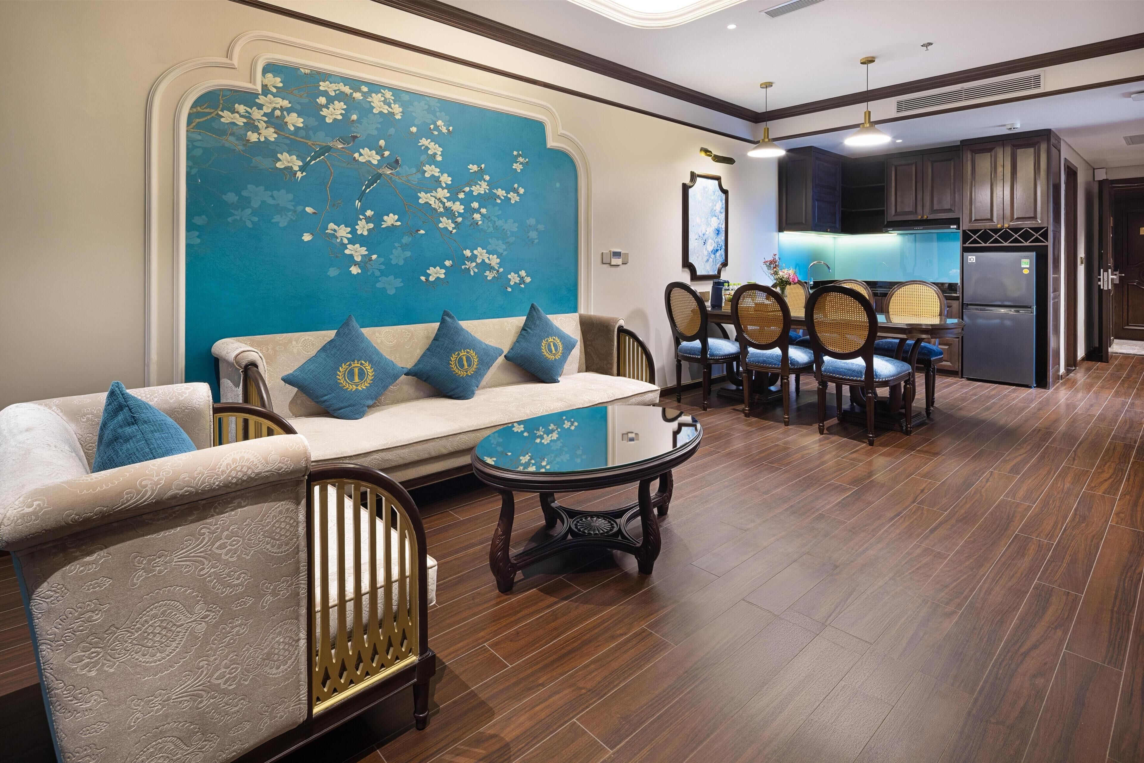 Sala de estar com sofá, cadeiras, mesa de centro e área de cozinha com armários e geladeira.
