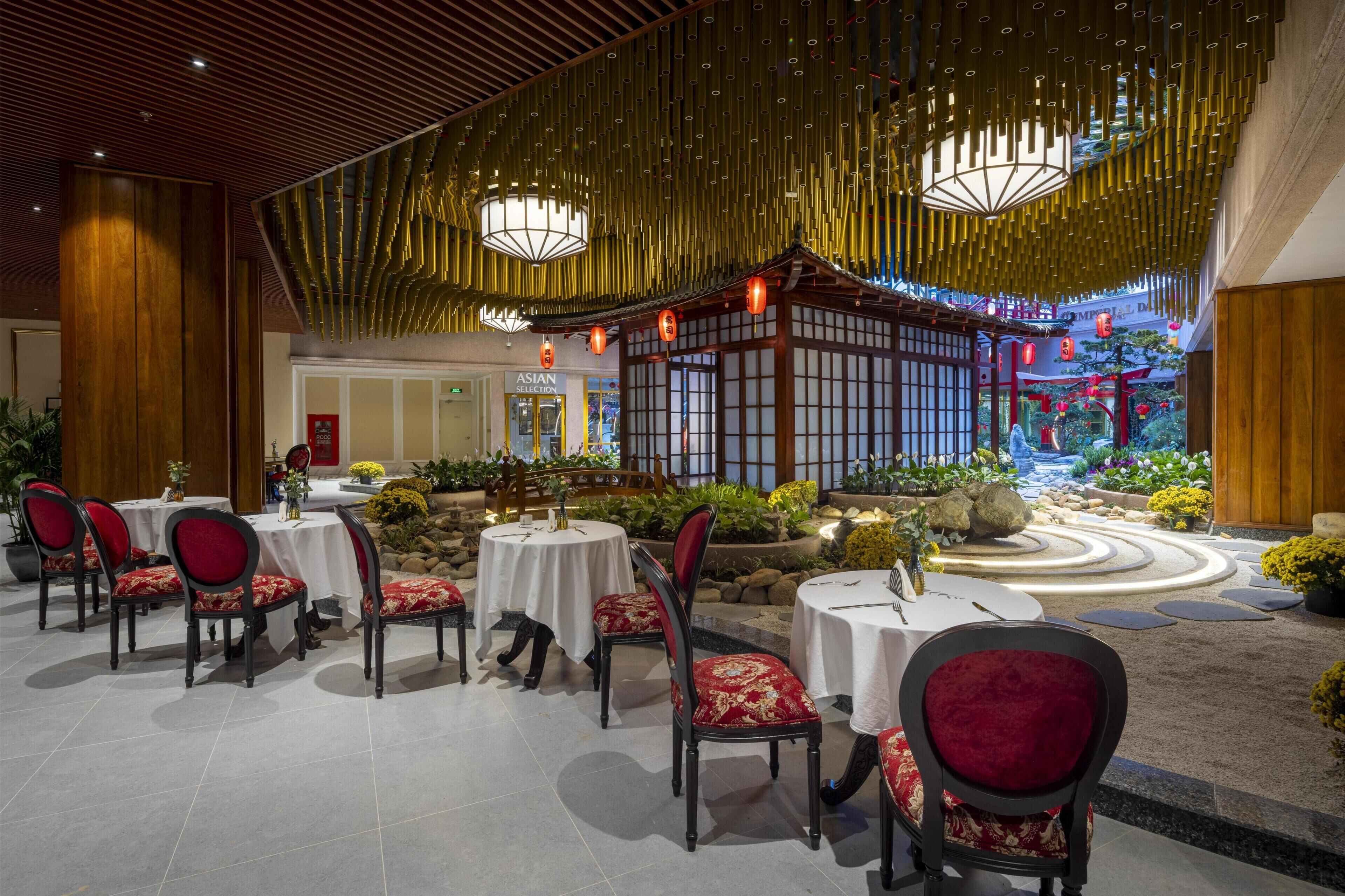 A restaurant with round tables and chairs, a traditional Asian-style building in the background, and a landscaped garden area.