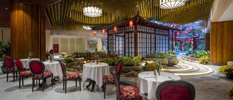 A restaurant with round tables and chairs, a traditional Asian-style building in the background, and a landscaped garden area.