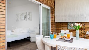 Ein modernes Hotelzimmer mit einem Bett, einer Essecke mit Tisch und Stühlen und Blick durch eine Glasdoor.