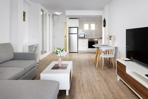 A modern living room with a grey sofa, a white coffee table with a vase, a dining area with a white table and chairs, and a kitchen in the background. - Seafront Escape by Alfresco Stays (Fuengirola)
