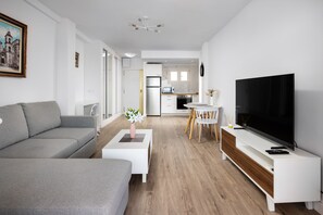 Ein modernes Wohnzimmer mit Sofa, Couchtisch, Fernseher und einem Essbereich mit Stühlen und Tisch.