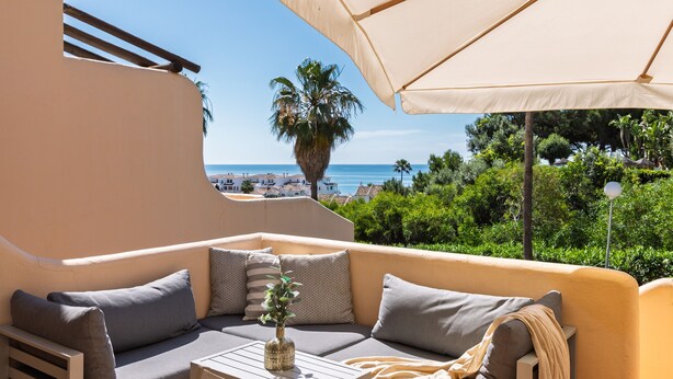 Un espacio al aire libre iluminado por el sol con vistas al mar, una palmera y una mesa con un florero.