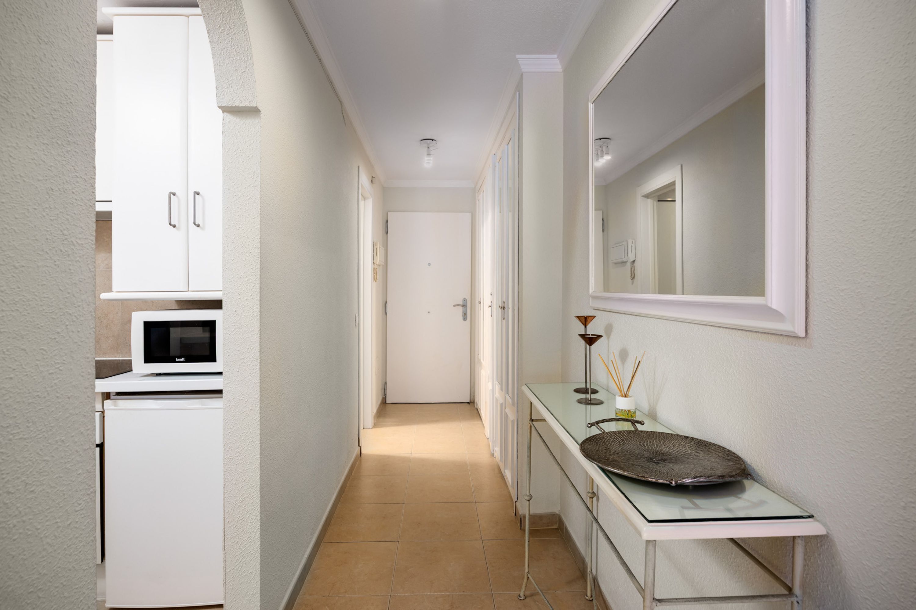 A narrow hallway with a microwave, cabinets, a sink, and a mirror.