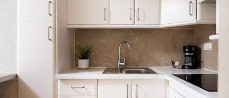 A modern kitchen with white cabinets, a stainless steel sink, a coffee maker, and a potted plant.