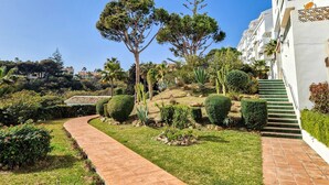 Um jardim ajardinado com um caminho curvo, uma árvore alta e um edifício com uma escadaria.