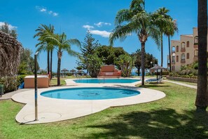 A pool area with palm trees, a lounge chair, and a building in the background. - AS SM 175 in Mijas Costa (Mijas)