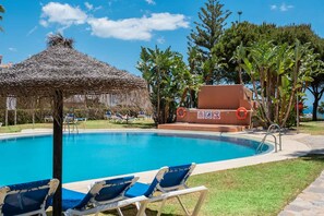 A swimming pool with lounge chairs, a thatched structure, and a lifeguard tower. - AS SM 175 in Mijas Costa (Mijas)