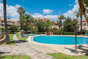 A swimming pool with lounge chairs, palm trees, and a clear blue sky. - AS SM 175 in Mijas Costa (Mijas)