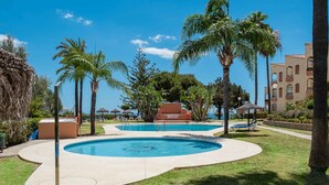 A pool area with palm trees, a lounge chair, and a building in the background. - AS SM 175 in Mijas Costa (Mijas)