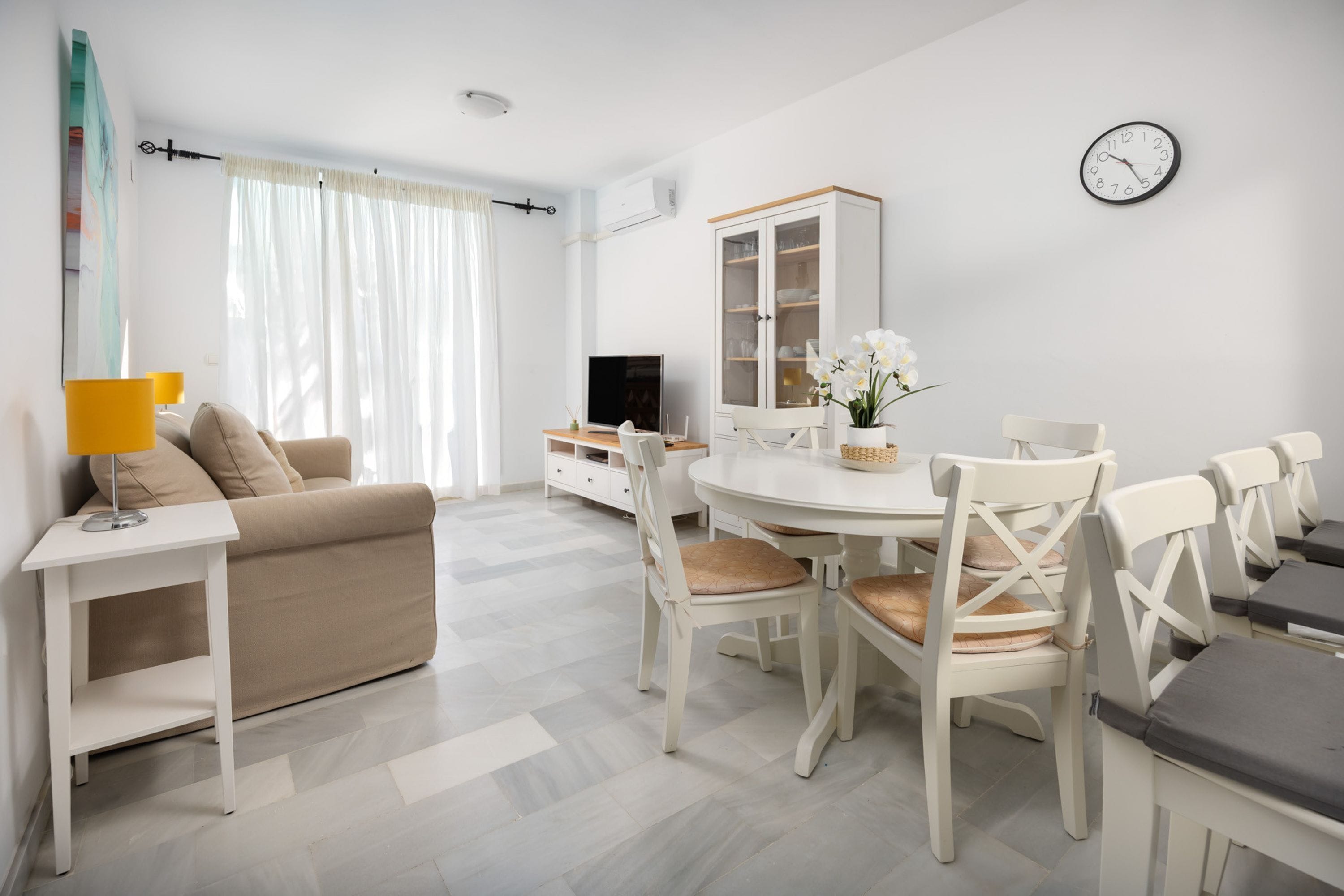 A living room with a sofa, dining table, chairs, a TV, and a cabinet.