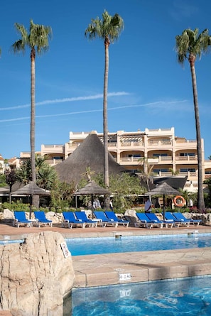 A pool area with lounge chairs, palm trees, and a building with balconies in the background. - AS MDM 10 in Mijas Costa (Mijas)