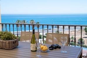 A balcony with a table set for two, featuring a bottle of wine, a glass, a bowl of fruit, and a basket of greenery. - AS MDM 10 in Mijas Costa (Mijas)