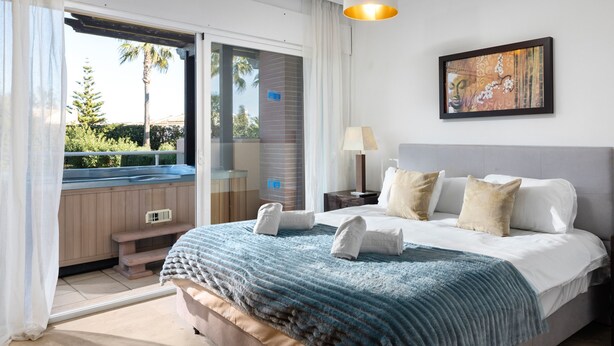 A bedroom with a bed, a nightstand, a lamp, a painting, and a view of a pool and greenery. - AS MM C02 in Mijas Costa (Mijas)
