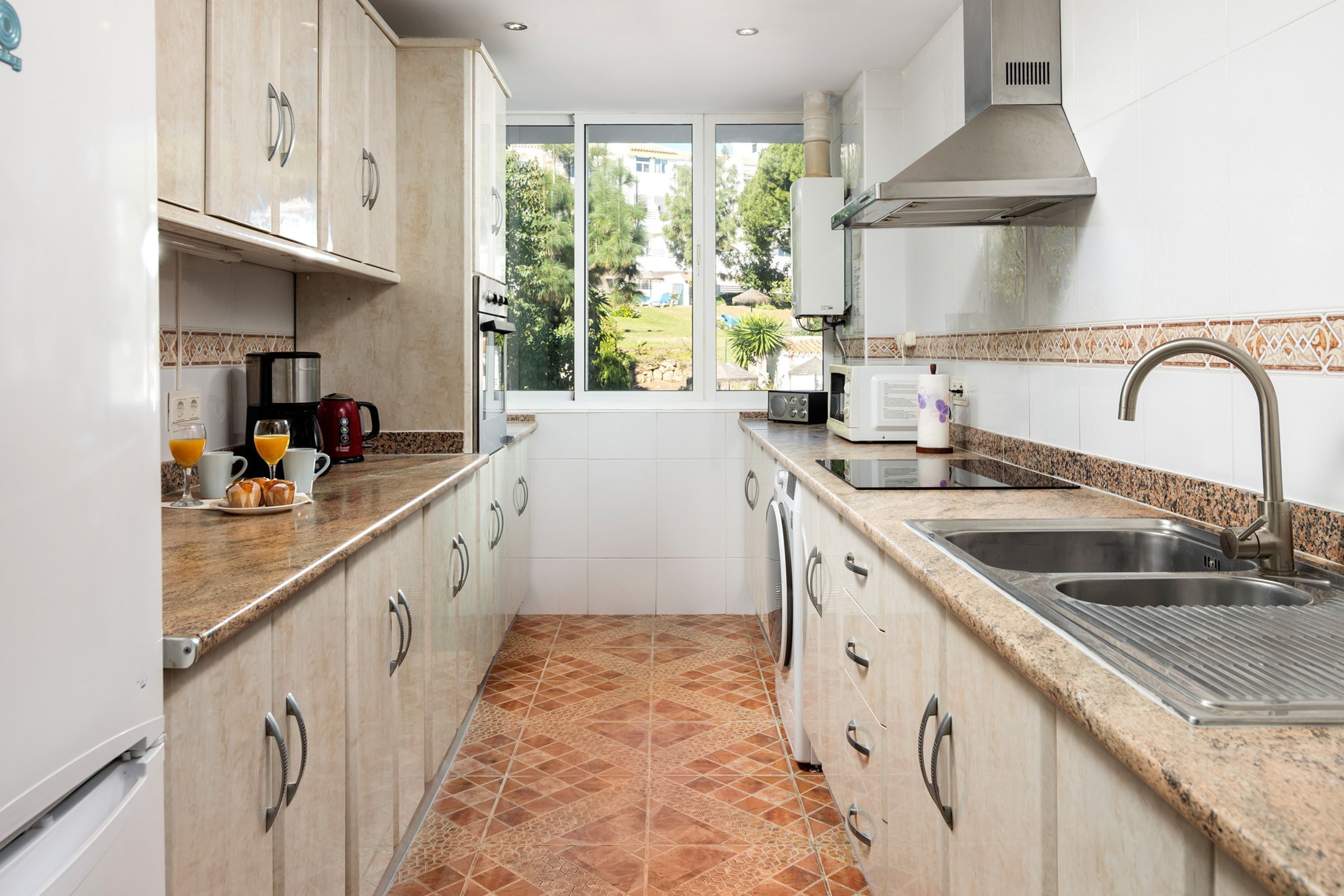 Cocina compacta con ventana, electrodomésticos de acero inoxidable y salpicadero de azulejos.