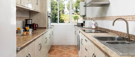 Cocina compacta con ventana, electrodomésticos de acero inoxidable y salpicadero de azulejos.