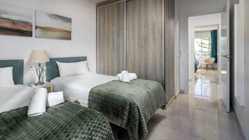 Een hotelkamer met twee bedden, een nachtkastje, een lamp, een grof geweven groene deken en een houten garderobe.