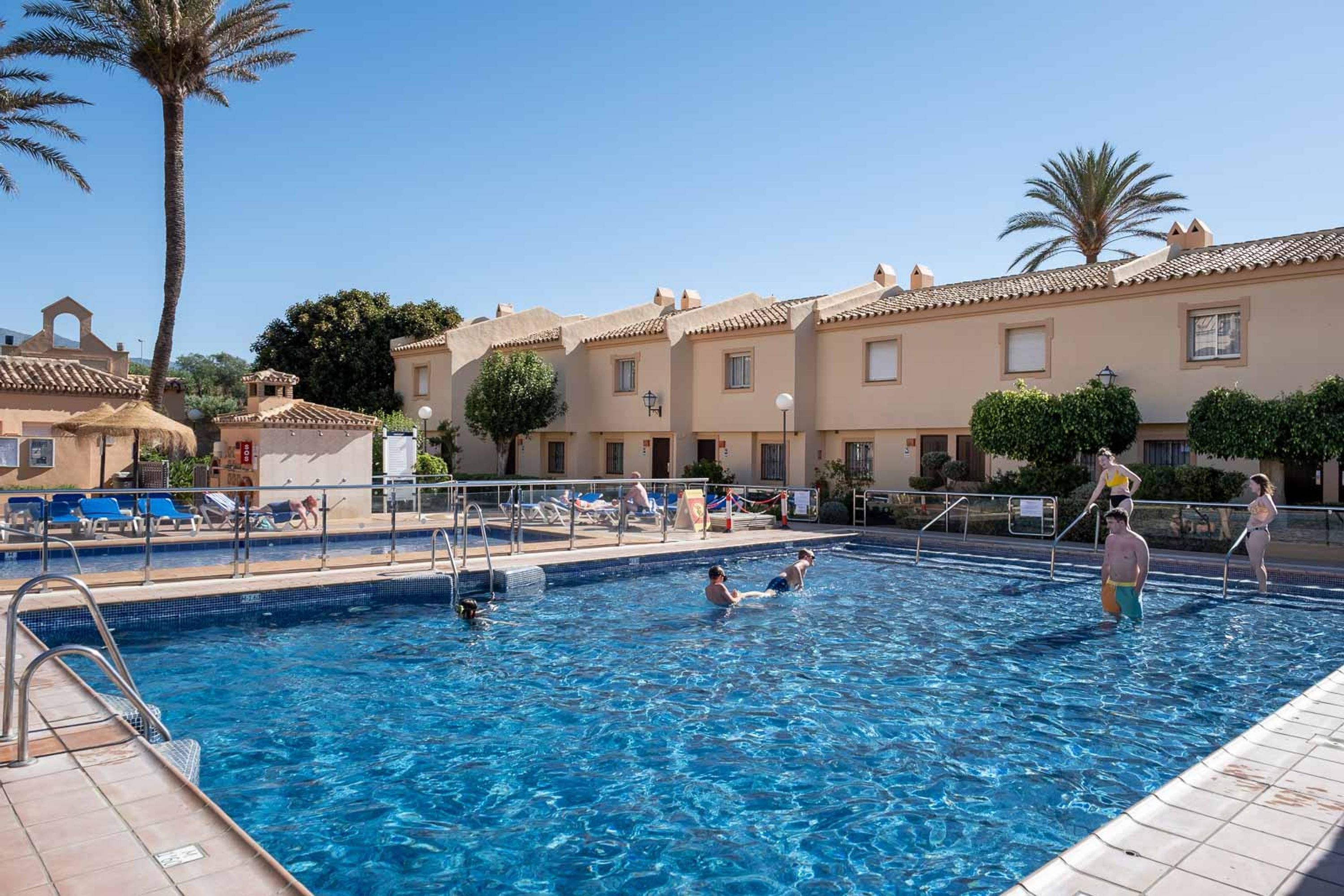 Una piscina con gente, rodeada de edificios y palmeras.