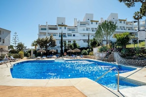 A swimming pool with lounge chairs and umbrellas, surrounded by buildings and palm trees. - AS MD 9B1 in Mijas Costa (Mijas)