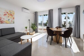 A modern living room with a sofa, a dining table with chairs, a potted plant, and a large window with curtains. - AS MD 9B1 in Mijas Costa (Mijas)