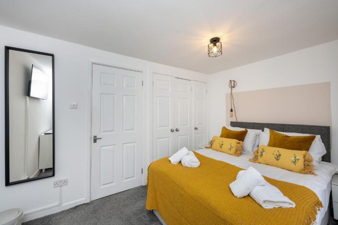 Une chambre d’hôtel avec un lit, des murs blancs, un grand miroir et un luminaire au plafond.