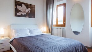 A bedroom with a bed, bedside tables, a window with curtains, a wall-mounted mirror, and a flower painting. - Apartments Florence - Boboli Balcony Rooftop View Florence City Center (Firenze)