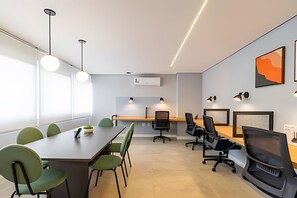 A modern meeting room with a long table, green chairs, black office chairs, pendant lights, and a large window. - Studio Mobiliado Próximo á Faria Lima  (São Paulo)
