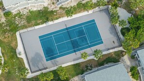 Vista aérea de una cancha de tenis rodeada de vegetación y edificios.