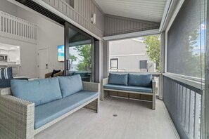 Ein überdachter Balkon mit Korbmöbeln und einem Fernseher.