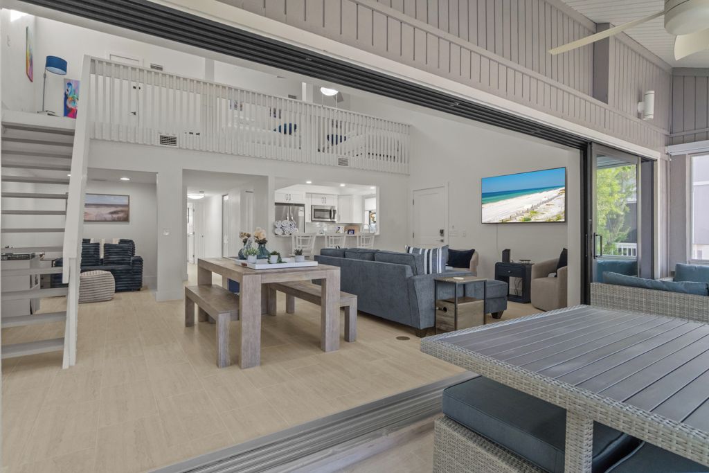 A spacious living area with a high ceiling, a dining table, sofas, and a kitchen in the background.