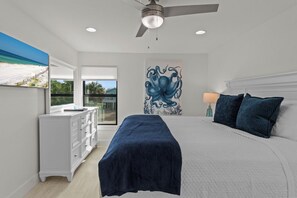 Ein Schlafzimmer mit einem Bett, einer weißen Kommode, einem Deckenventilator, einem Bild von einem Oktopus und einem Fenster mit Blick.