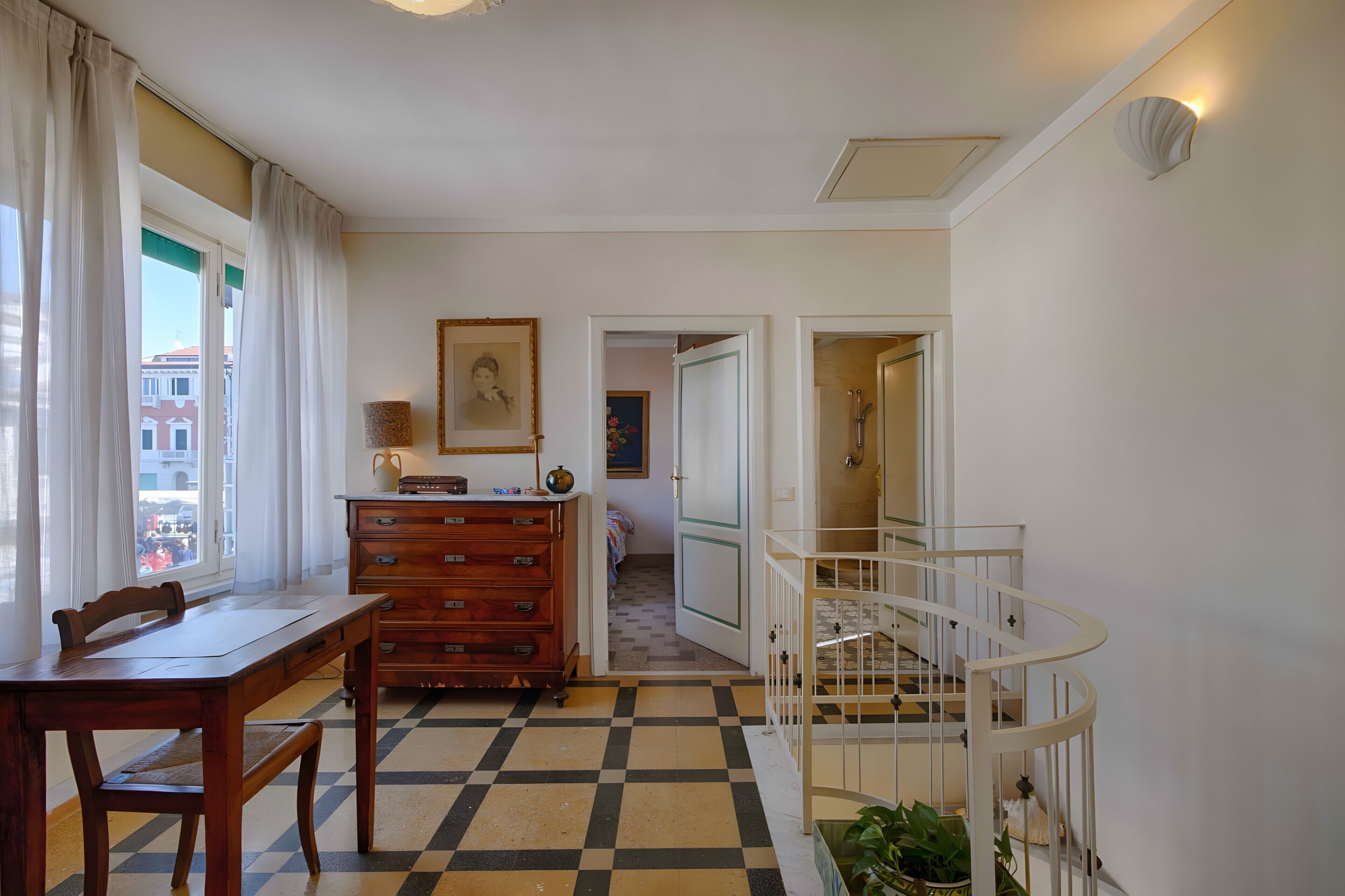 A room with a checkered floor, a wooden dresser, a white crib, and a view of buildings outside.