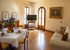 A dining area with a table set for two, a television, and a painting on the wall. - Apartment 'Casa Del Tato Central  - 2' with Wi-Fi (Lucca)