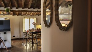 Ein rustikales Interieur mit freiliegenden Holzbalken, einem Essbereich mit Tisch für vier Personen und einer Küche im Hintergrund.